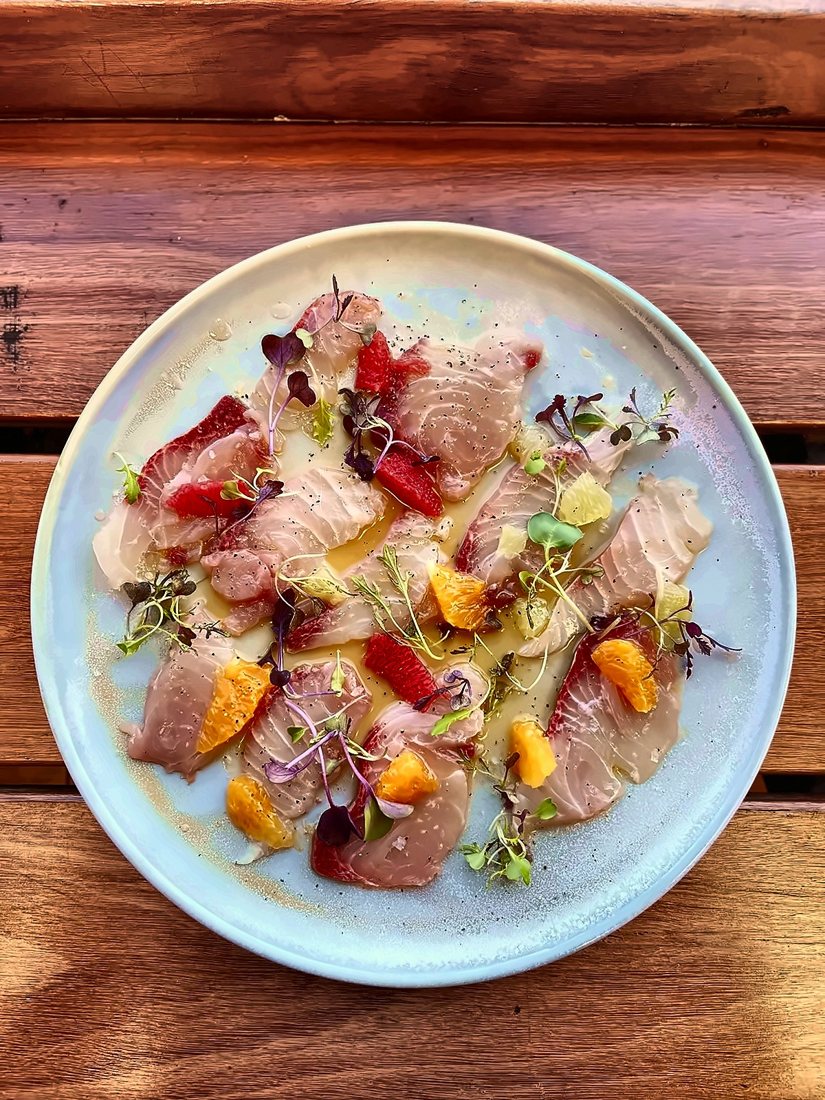 A plate of thinly sliced raw fish with citrus and micro herbs